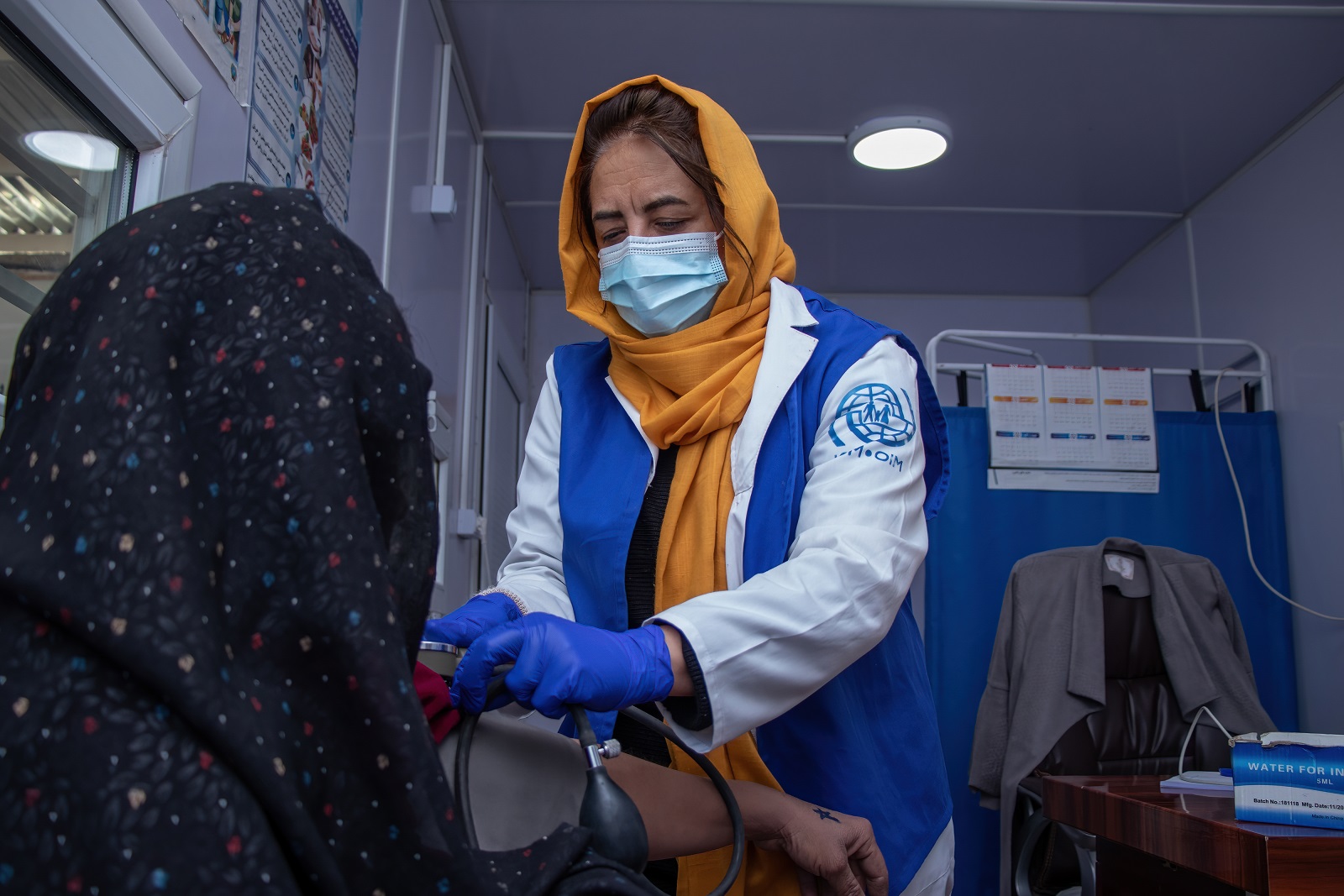 Kansainvälisen siirtolaisuusjärjestön takkiin pukeutunut lääkäri mittaa afganistanilaisen naisen verenpainetta.