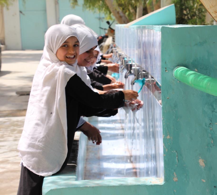 Girls washing their hands under a tap.