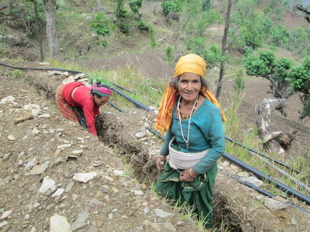 Kaksi naista kaivaa syvälle maahan linjaa vesitputkea varten.