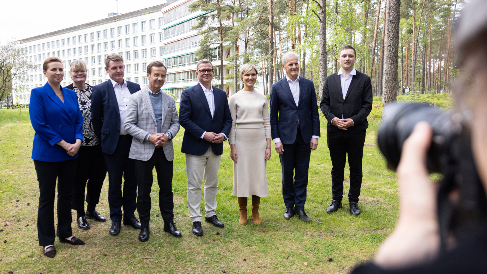 Nordiska ländernas regeringschefer står uppradade för fotografering. I bakgrunden syns byggnaden för Paimio sanatorium. På bildens högra sida syns en annan fotografs hand och kamera.