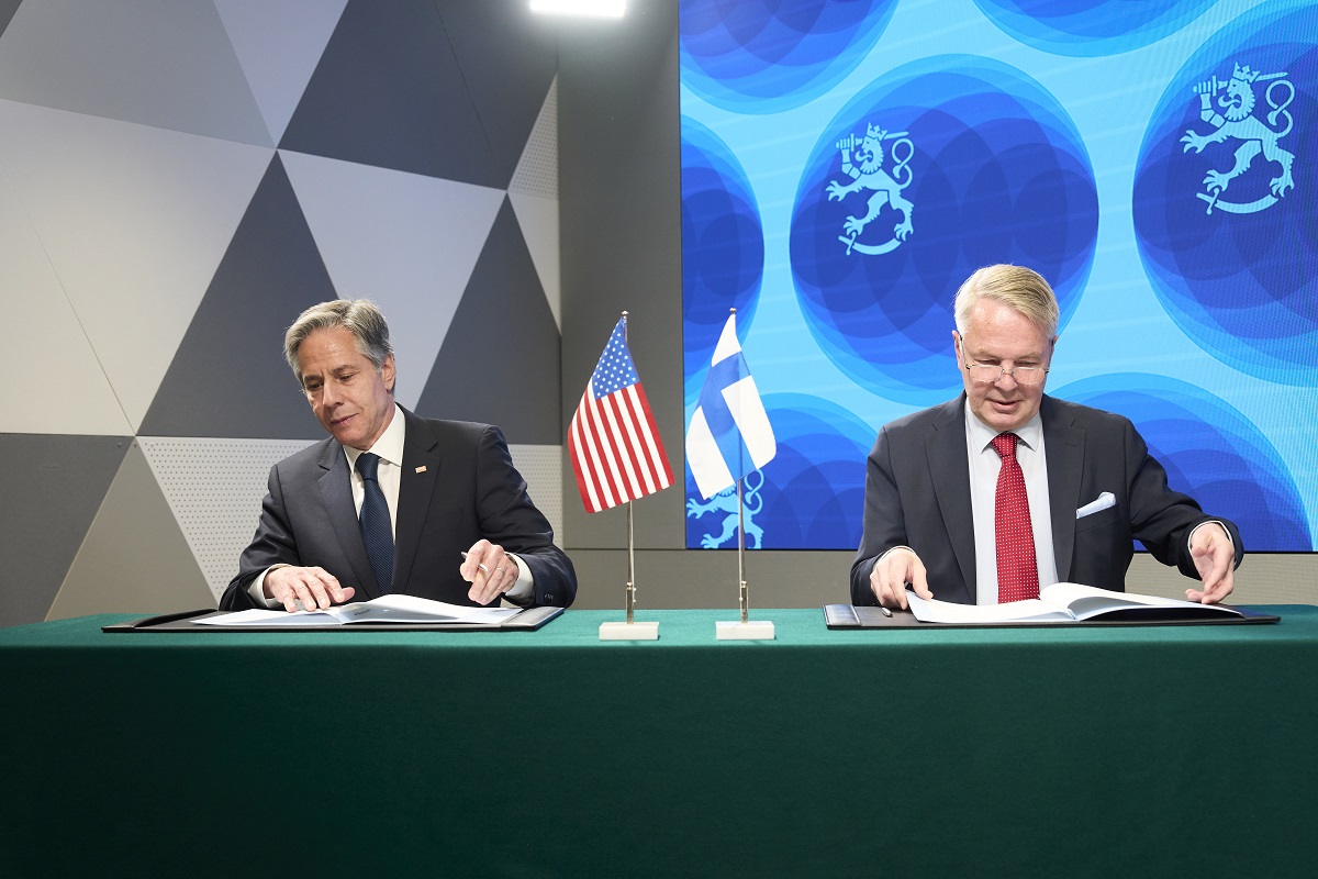 Kuvassa vasemmalla USAn ulkoministeri Blinken ja oikealla ulkoministeri Pekka Haavisto. Molemmat istuvat pöydän ääressä kansiot edessään, käsissään kynä. Keskellä USAn ja Suomen pöytäliput.
