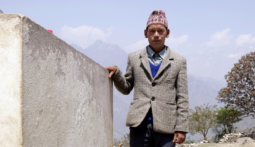 Dilip Sing Dhami posing for the camera next to a water tank.
