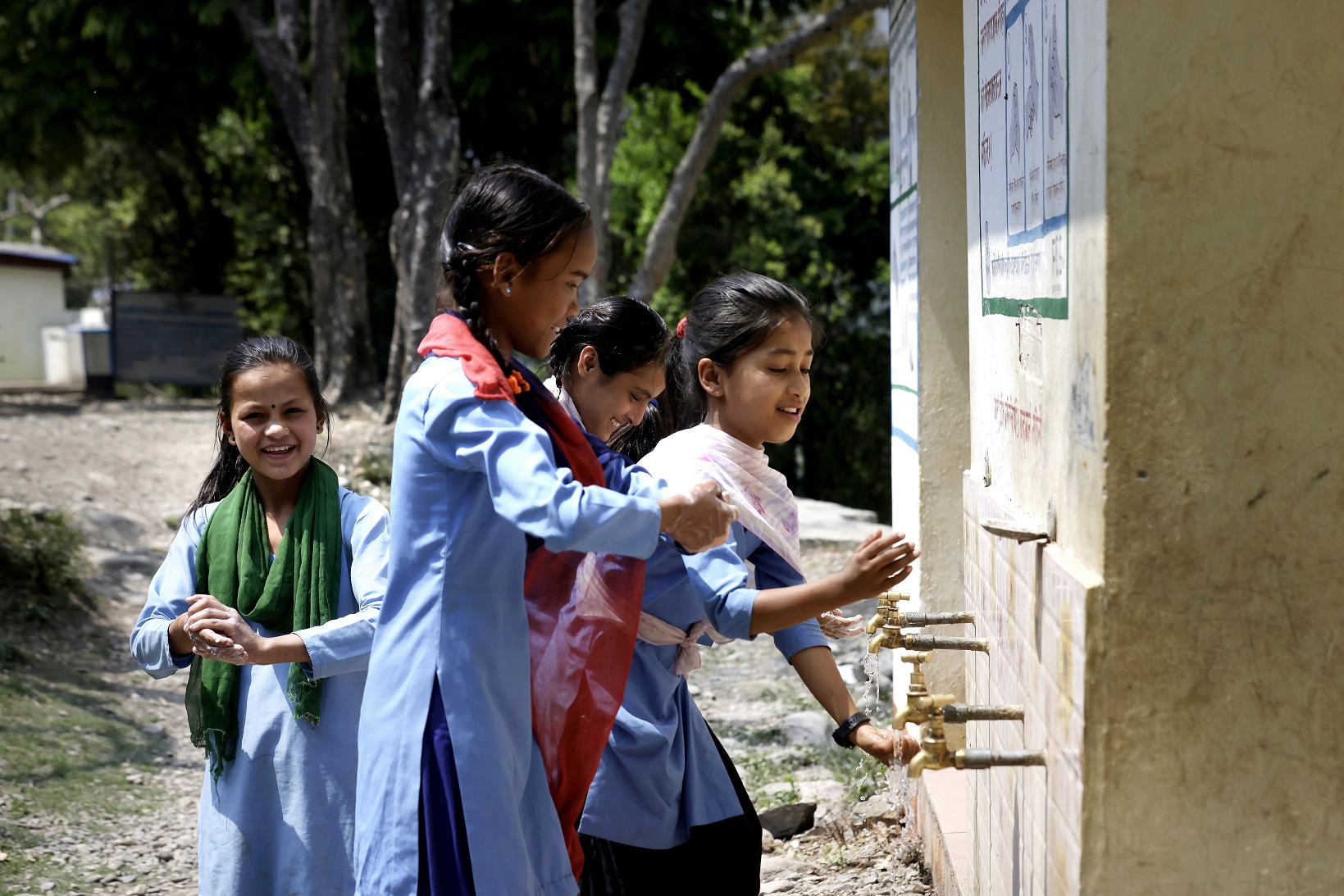 Four children washing their hands at an outdoor water point.