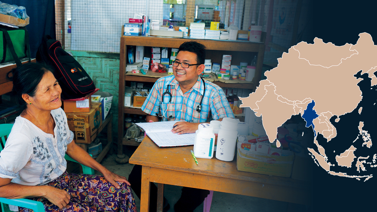 A refugee woman is sitting at the same table with a male doctor at a mobile clinic. Also pictured is a map of Asia marked with Myanmar