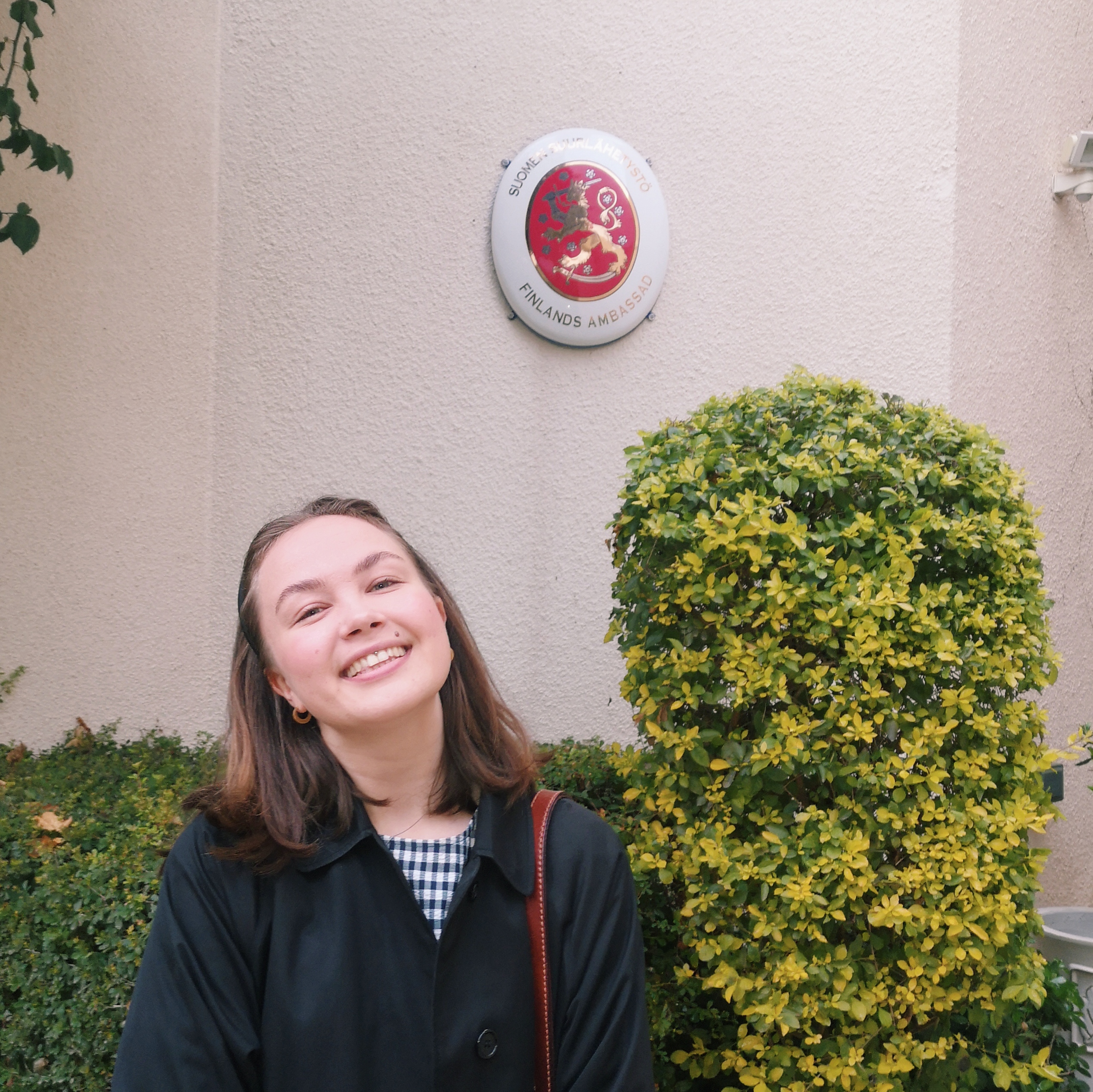 A young woman smiles and poses in front of the Finnish emblem.