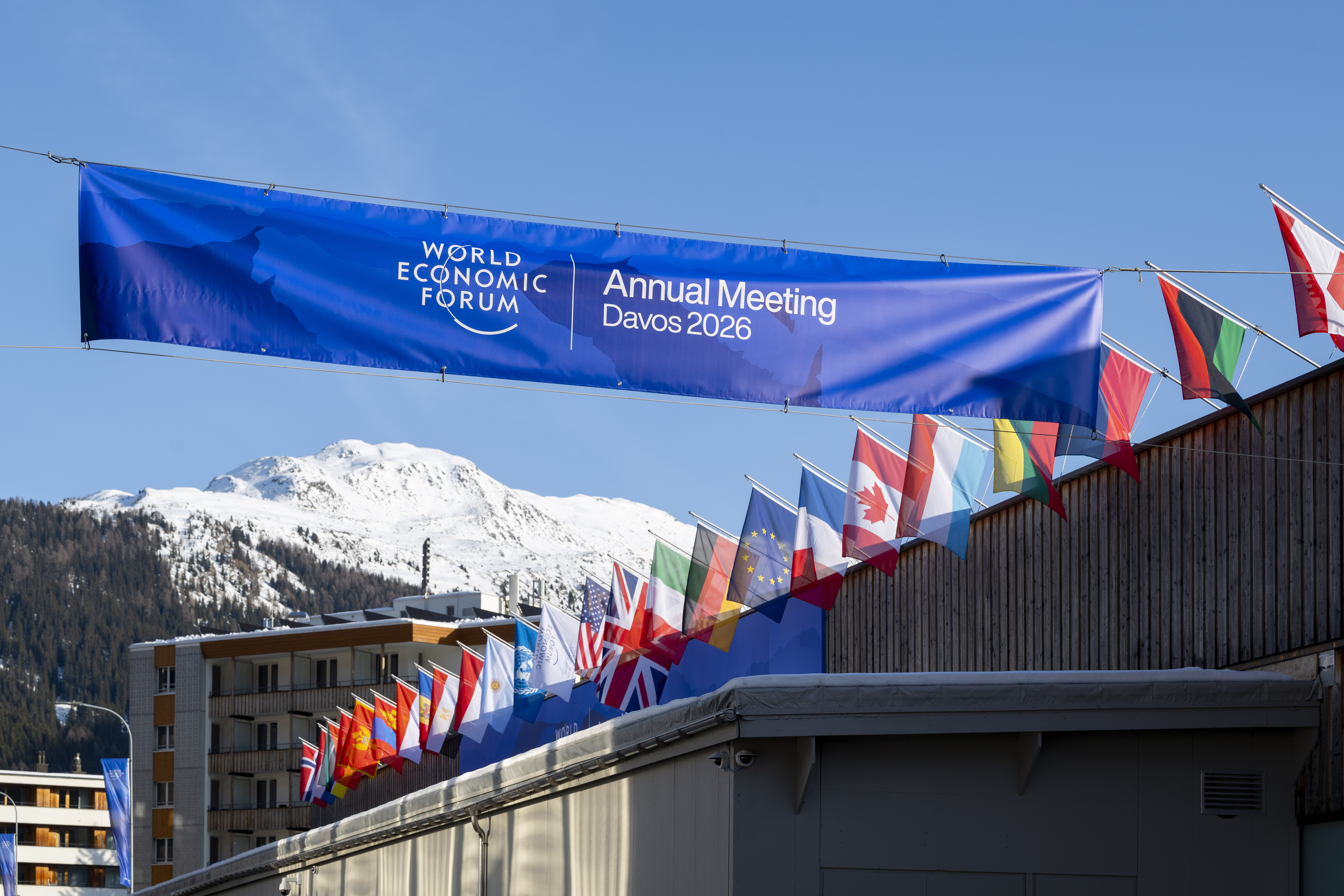 World Economic Forum 2026-Banneri, jonka takana useiden maiden lippuja. Taustalla lumipeitteinen vuori.