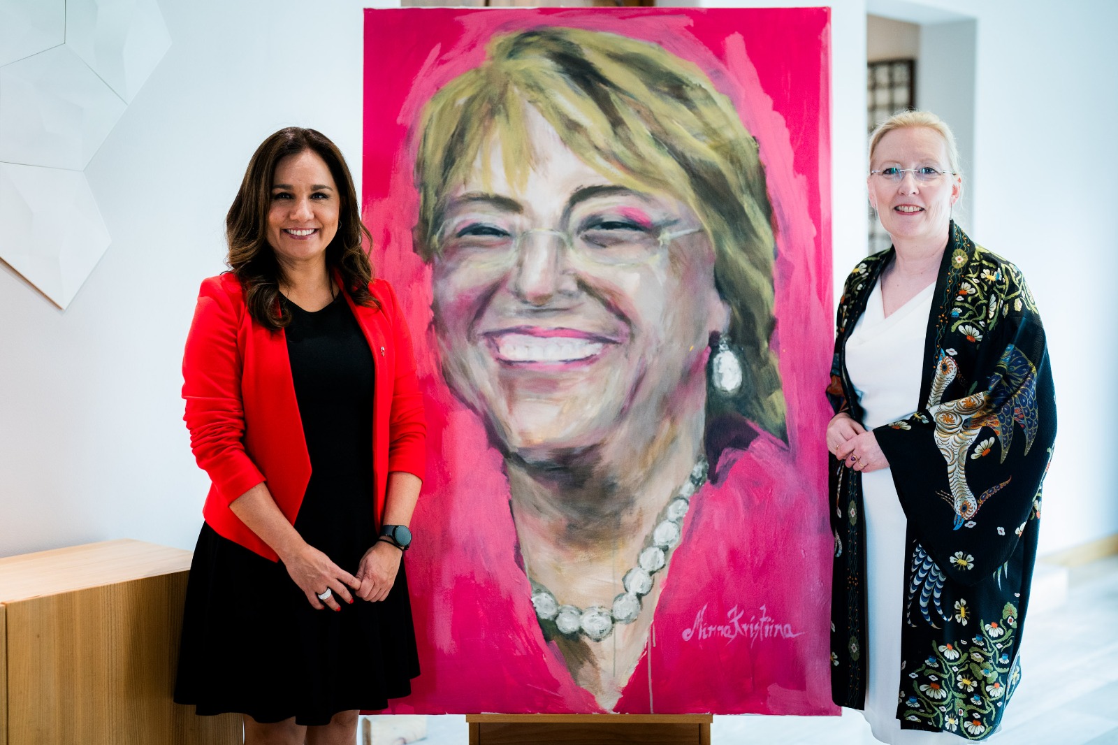 Subsecretaria Gloria de la Fuente y Embajadora de Finlandia Johanna Kotkajärvi junto al retrato de Michelle Bachelet