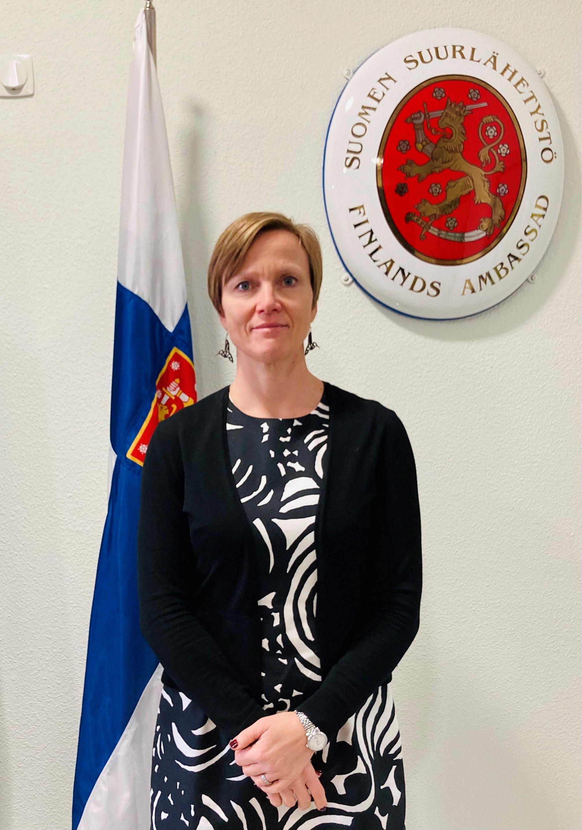 Suomen Espanjan-suurlähettiläs Sari Rautio, Suomen lipun ja suurlähetystön vaakunan edessä