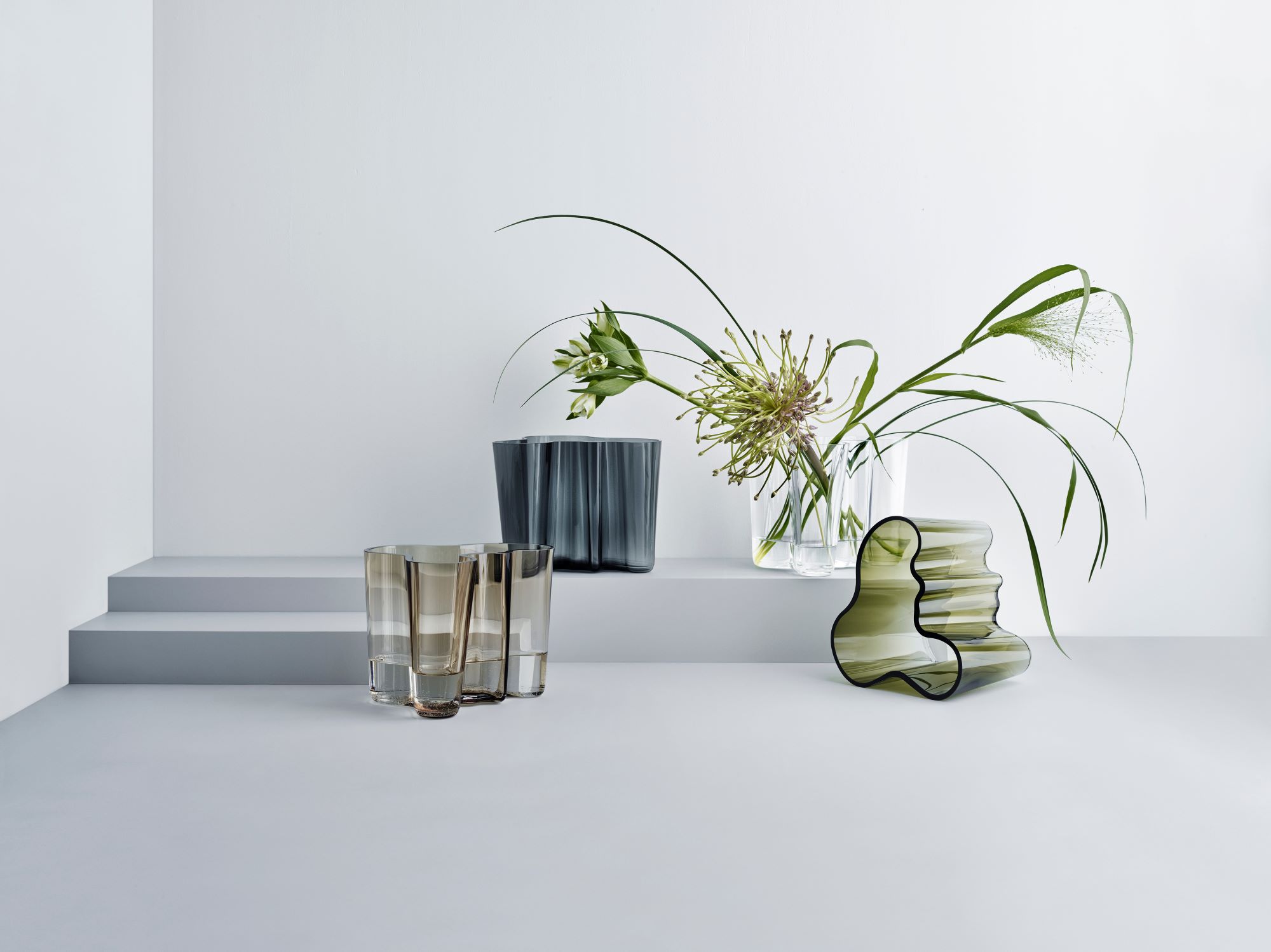 Green, grey, clear and linen-colored Aalto vases, with one of them holding flowers.