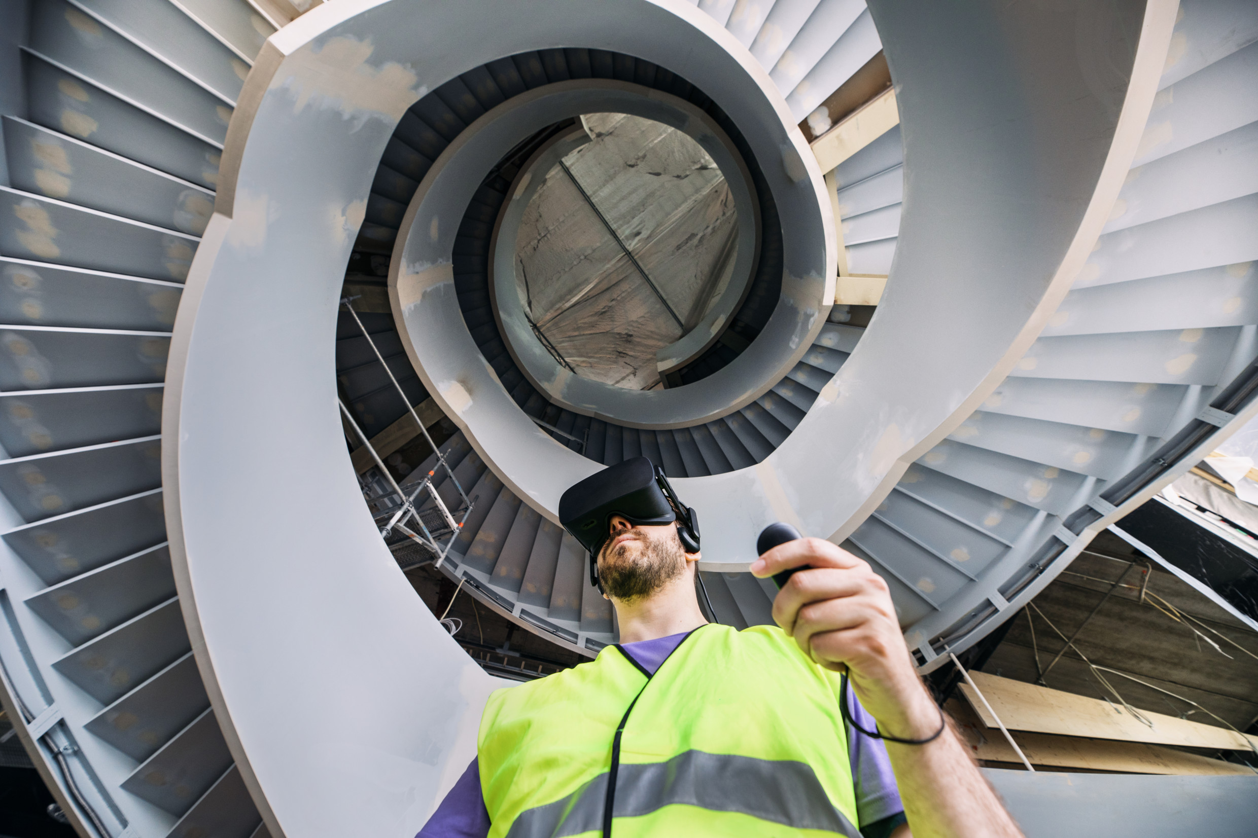 A bearded person wearing a VR headset and a safety reflector vest in the middle of a circular staircase
