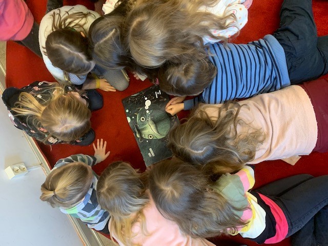 Ryhmä lapsia lattialla ringissä polvillaan lukemassa kuvakirjaa.