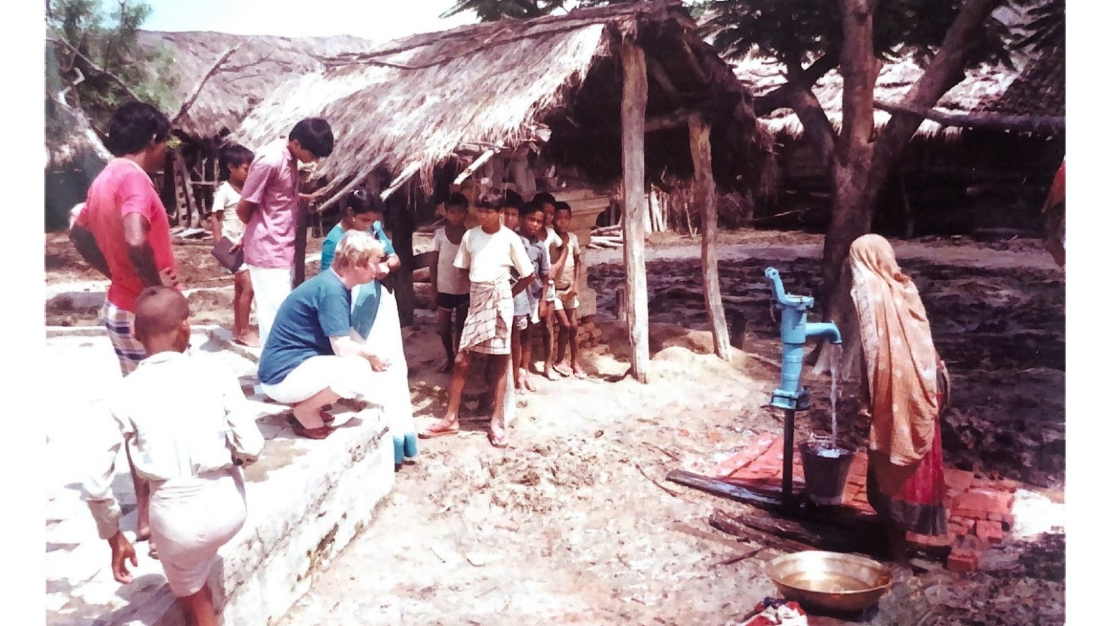 There is a woman using a water tap and plenty of kids are around watching, among them a Finnish WASH expert from the Lumbini Project.