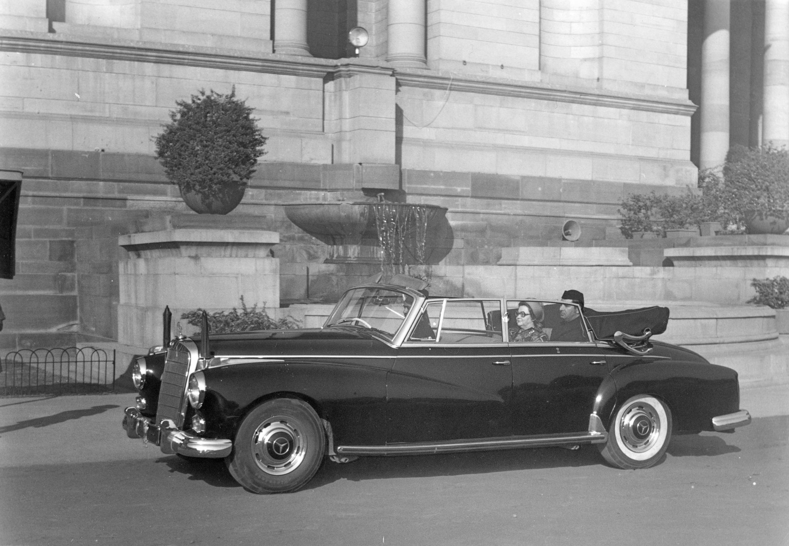 Image of Ms. Riitta Örö, Finland's Ambassador to India, sitting on the backseat of a stylish black convertible car. There is a man, Indian diplomat, sitting next to Ms. Riiitta Örö.