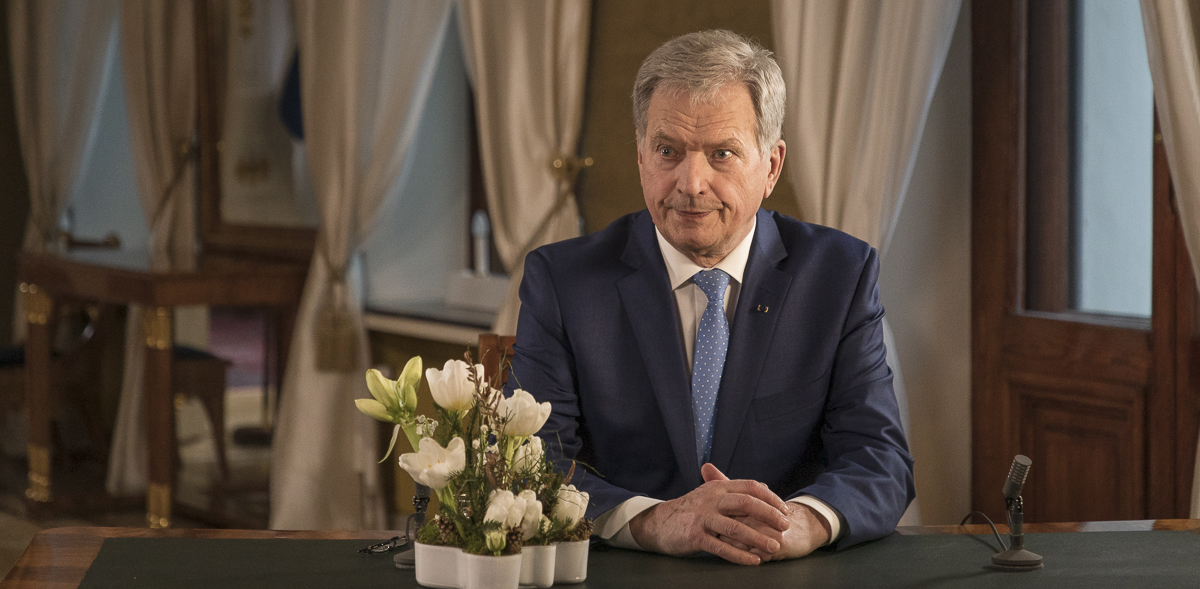Presidentti Niinistö istuu kirjoituspöydän ääressä, valkoinen kukkakimppu pöydällä.