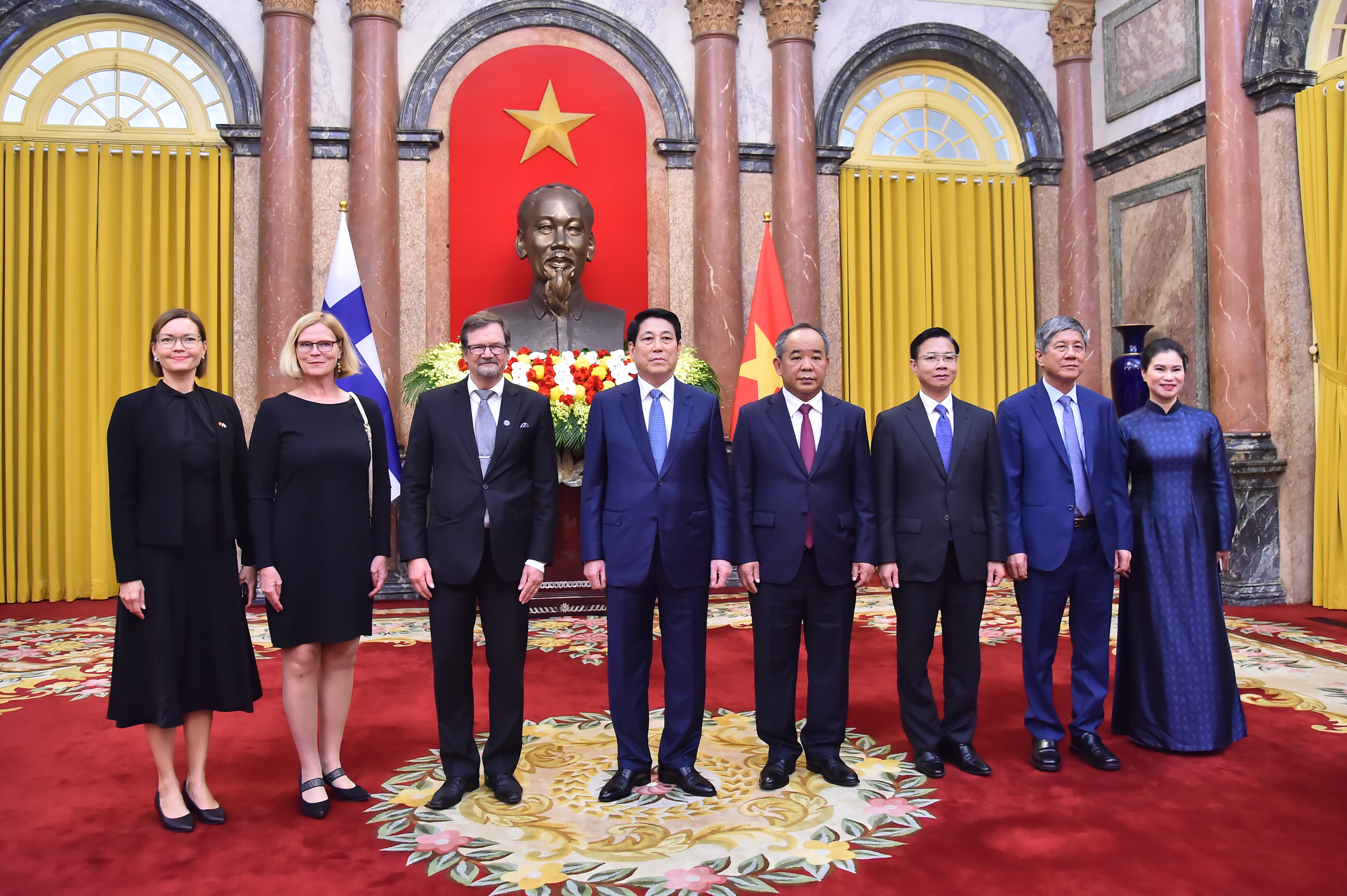 Ảnh chụp nhóm 8 người ở phía trước mặc trang phục tối màu, từ trái sang phải là hai phụ nữ Phần Lan, sau đó là 5 quý ông và một phụ nữ mặc trang phục truyền thống Việt Nam đứng ngoài cùng bên phải.