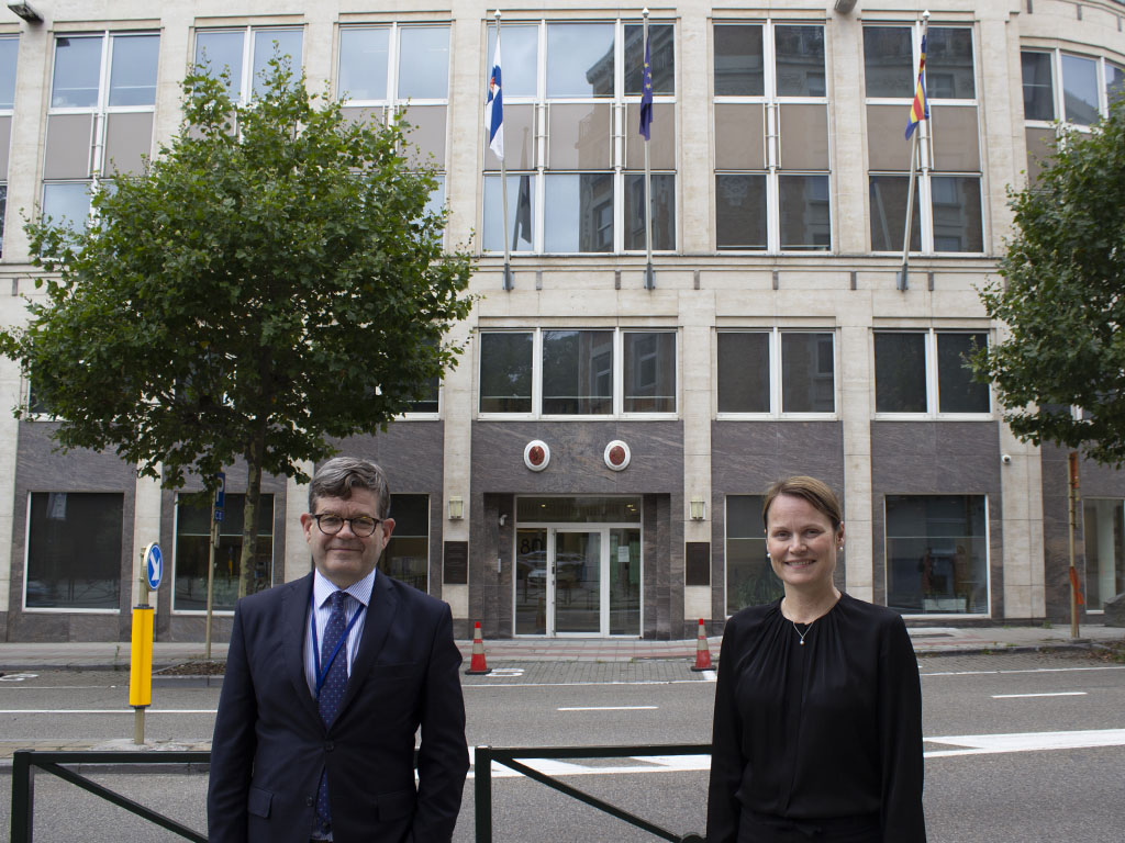 Markku Keinänen ja Tuuli-Maaria Aalto seisovat Suomen EU-edustuston ja Brysselin suurlähetystön edessä. Takana kaksi puuta ja autotie. 