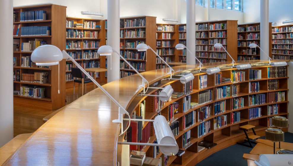 Biblioteksinteriör med böjda bokhyllor och läslampor.
