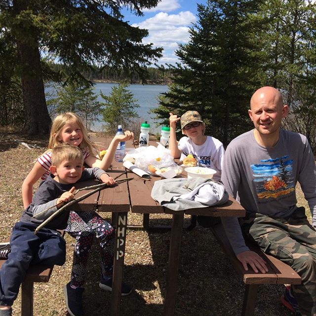 Mies ja kolme lasta istuvat piknik-pöydän ympärillä.